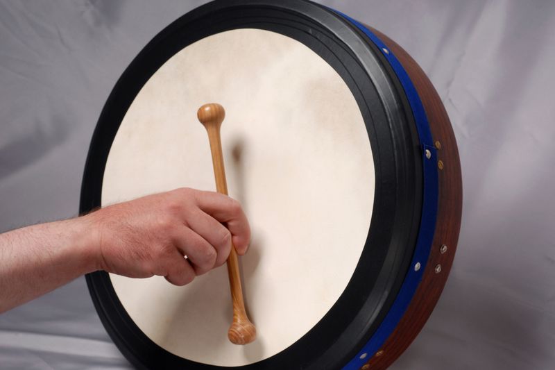 A hand striking a bodhrán’s goatskin head with a wooden tipper