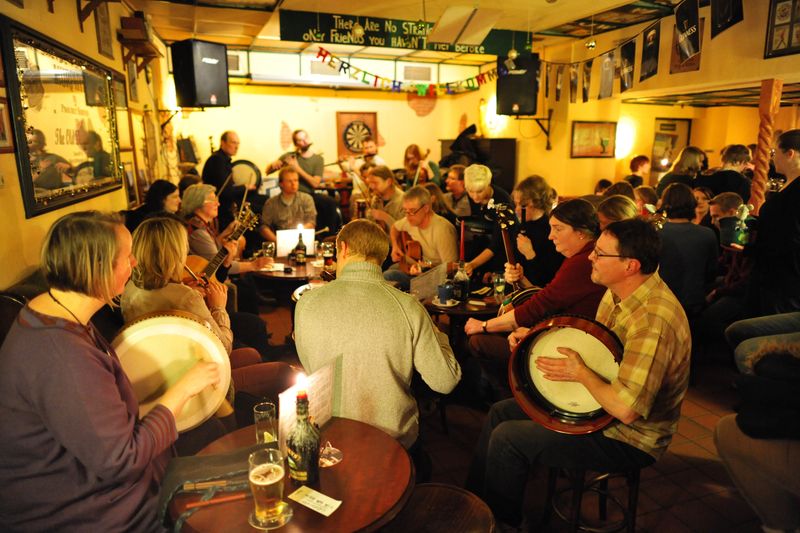 Musicians with fiddles, guitars and bodhráns playing together at an Irish traditional music session in a pub